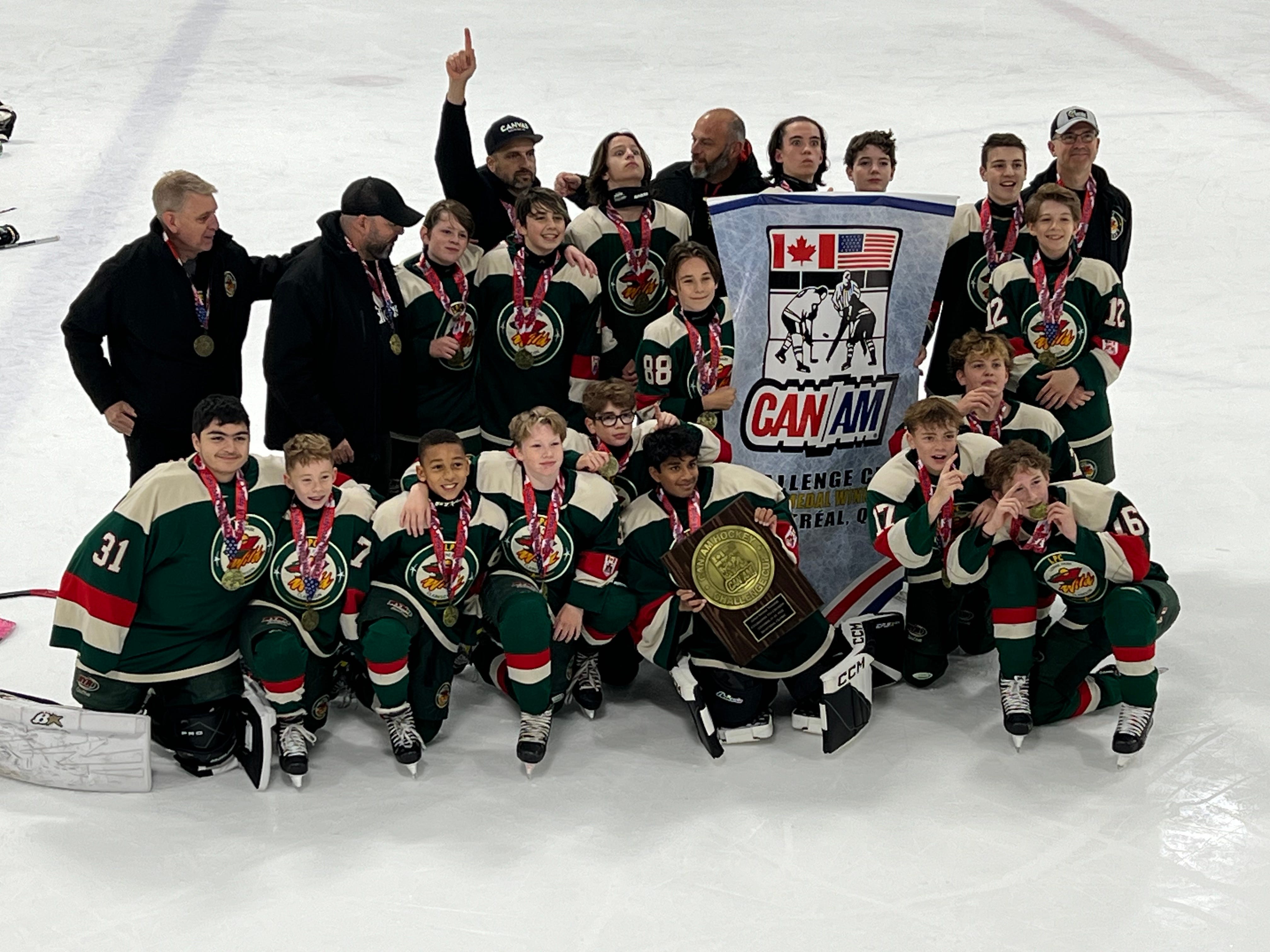 A youth hockey team in green jerseys posing on the ice with medals, a plaque and a CAN/AM Challenge Cup banner
