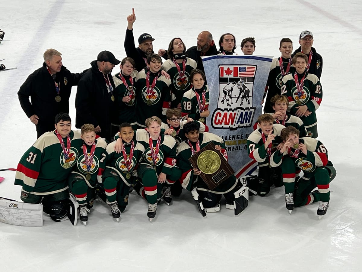 A youth hockey team in green jerseys posing on the ice with medals, a plaque and a CAN/AM Challenge Cup banner